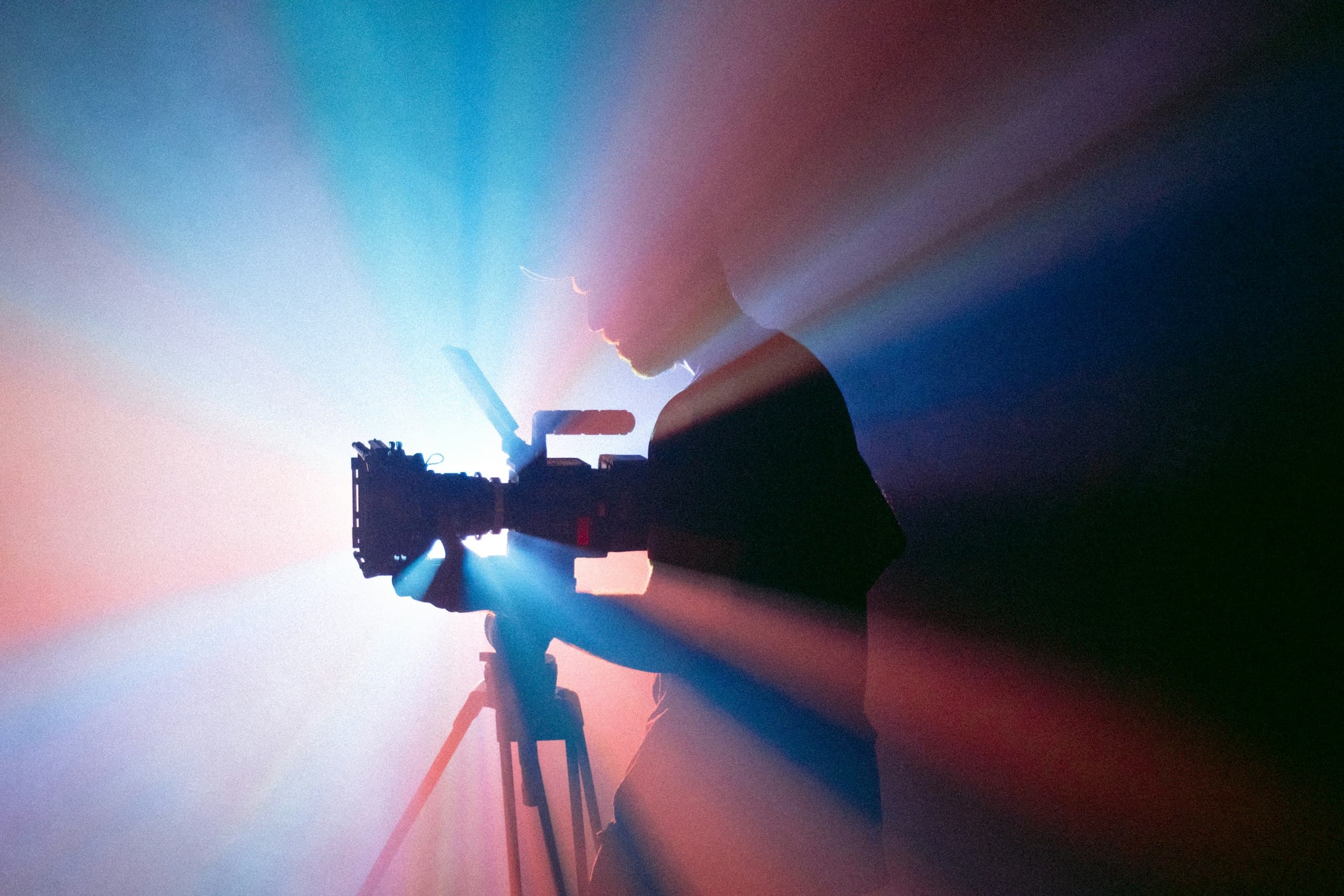 Filmmaker behind a camera, backlit by coloured light